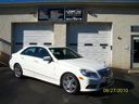White coupe parked in front of a garage and brick house.