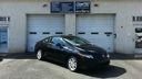Black sedan parked in front of white garage doors with a blue sign above.