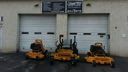 Orange lawn mowers lined up in front of two white garage doors at a storefront