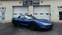 Blue sports car parked outside a building with garage doors and a shop entrance