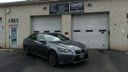 Dark sedan parked in front of a building with garage doors and a red awning