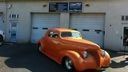 Orange vintage car parked in front of a garage with closed white doors.