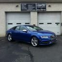 Blue sedan parked in front of a garage with two white doors