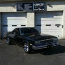 Black classic car parked in front of two garage doors on a storefront street.