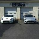 Two white sports cars parked side by side in front of garage doors