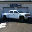 White pickup truck parked in front of a building with dark windows and a garage door