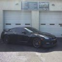 Black sports coupe parked outside a garage with white roll-up doors and signs above them