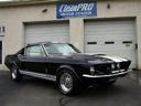 Black classic muscle car parked in front of a garage with a sign above the door