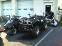 Three motorcycles and a black three-wheeled trike parked in front of garage doors