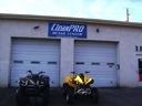 Two motorcycles parked in front of a building with three garage doors and a blue sign above them