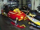Red and black race cars displayed indoors, with bright yellow graphics and a large star on one car.
