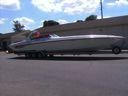 Long silver boat on a trailer with flashing lights, parked outdoors under a blue sky