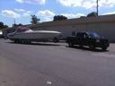 Black truck towing a large white trailer across an open parking lot under a blue sky