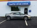 Silver sports coupe parked outside a clean car center with a blue sign.