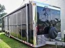 Transparent-sided mobile greenhouse trailer with plants inside, parked on grass outdoors