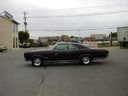 Black coupe parked in a lot beside a beige building under an overcast sky