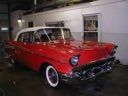 Red vintage car parked indoors beside a white vehicle