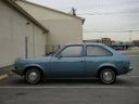 Blue vintage car parked beside a beige building and fence