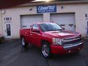 Red pickup truck parked in front of a garage with open service bays.