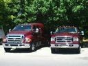 Two red fire trucks parked side by side on a road under trees