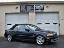 Black BMW coupe parked outside a garage with white doors and business signs above