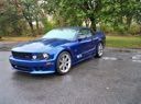 Blue sports car parked on a road beside trees and grass