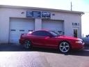 Red sports coupe parked outside a garage with white doors and service signs above it.