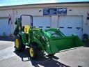 Green tractor with front loader parked outside a building with garage doors