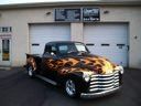 Classic car with orange flame paint parked in front of a garage