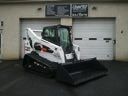 White skid-steer loader with a bucket parked in front of a garage door