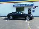 Black sedan parked outside a blue auto service center under a clear sky