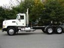 White semi-truck with flatbed trailer and three axles driving on a road, side view