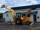 Yellow backhoe loader parked outside a building with a blue door and white walls.