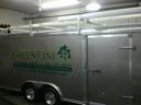 Silver enclosed trailer with green logo parked in a garage or workshop