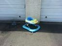 Blue and white baby walker on a concrete surface in front of a garage door