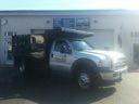 Silver pickup truck at a gas station pump with a person standing beside it