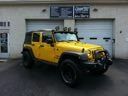 Yellow off-road Jeep parked outside a garage, with a white truck in the background.
