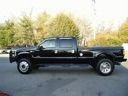 Black pickup truck parked outdoors on a paved surface, side view with trees in the background