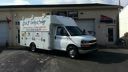 White box truck parked outside a small building with an open garage door.