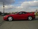 Red sports car parked on a paved lot under a cloudy sky.