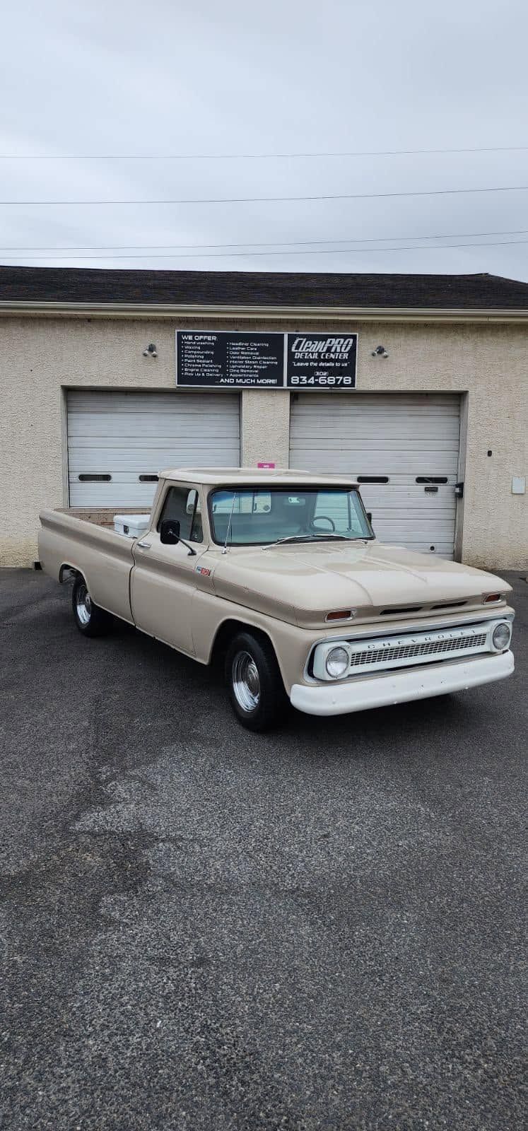 Beige vintage pickup truck parked in front of a garage under an overcast sky.