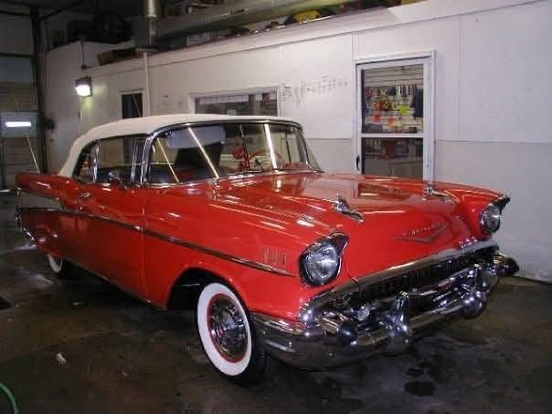 Red classic car with whitewall tires parked indoors in a garage or showroom.