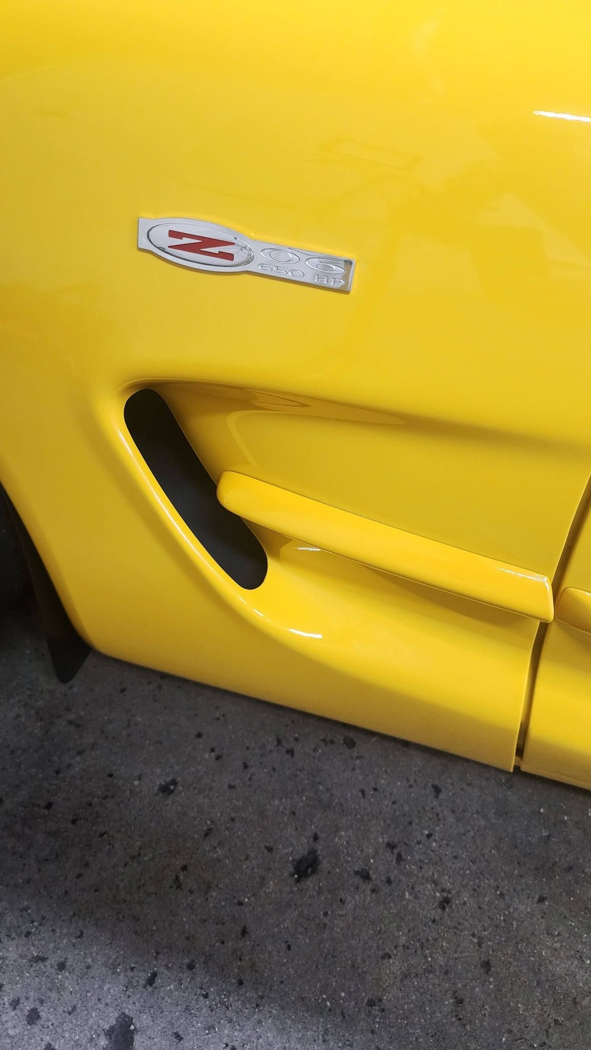 Yellow sports car side panel with black air vent and Corvette badge close-up