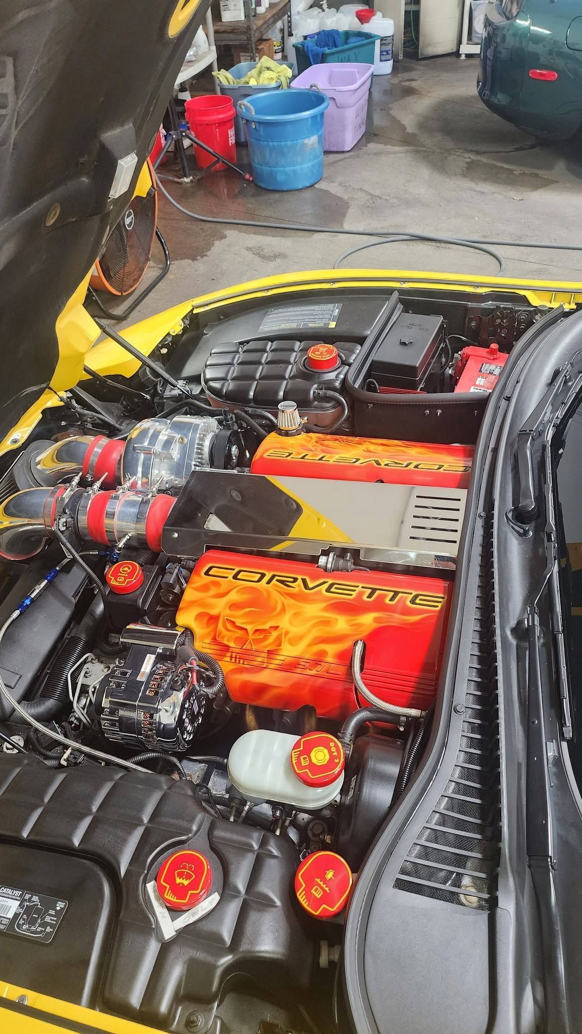 Bright yellow sports car with exposed engine in a garage, surrounded by buckets and tools.