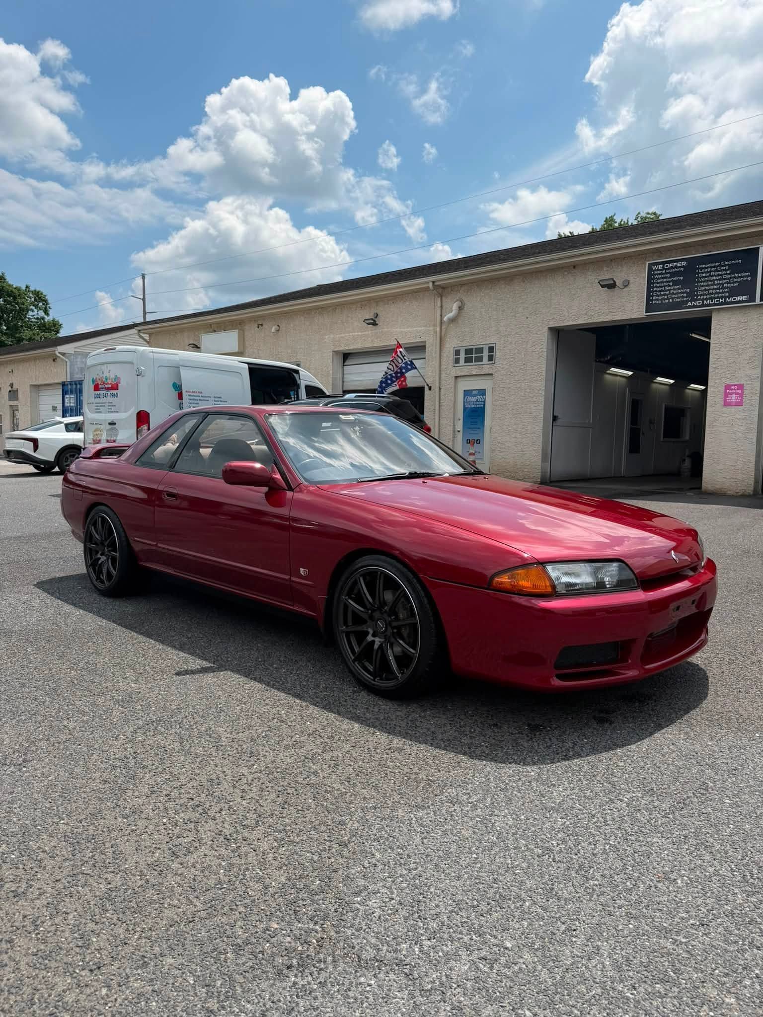 Maroon sedan parked on gravel outside an auto shop under a partly cloudy sky
