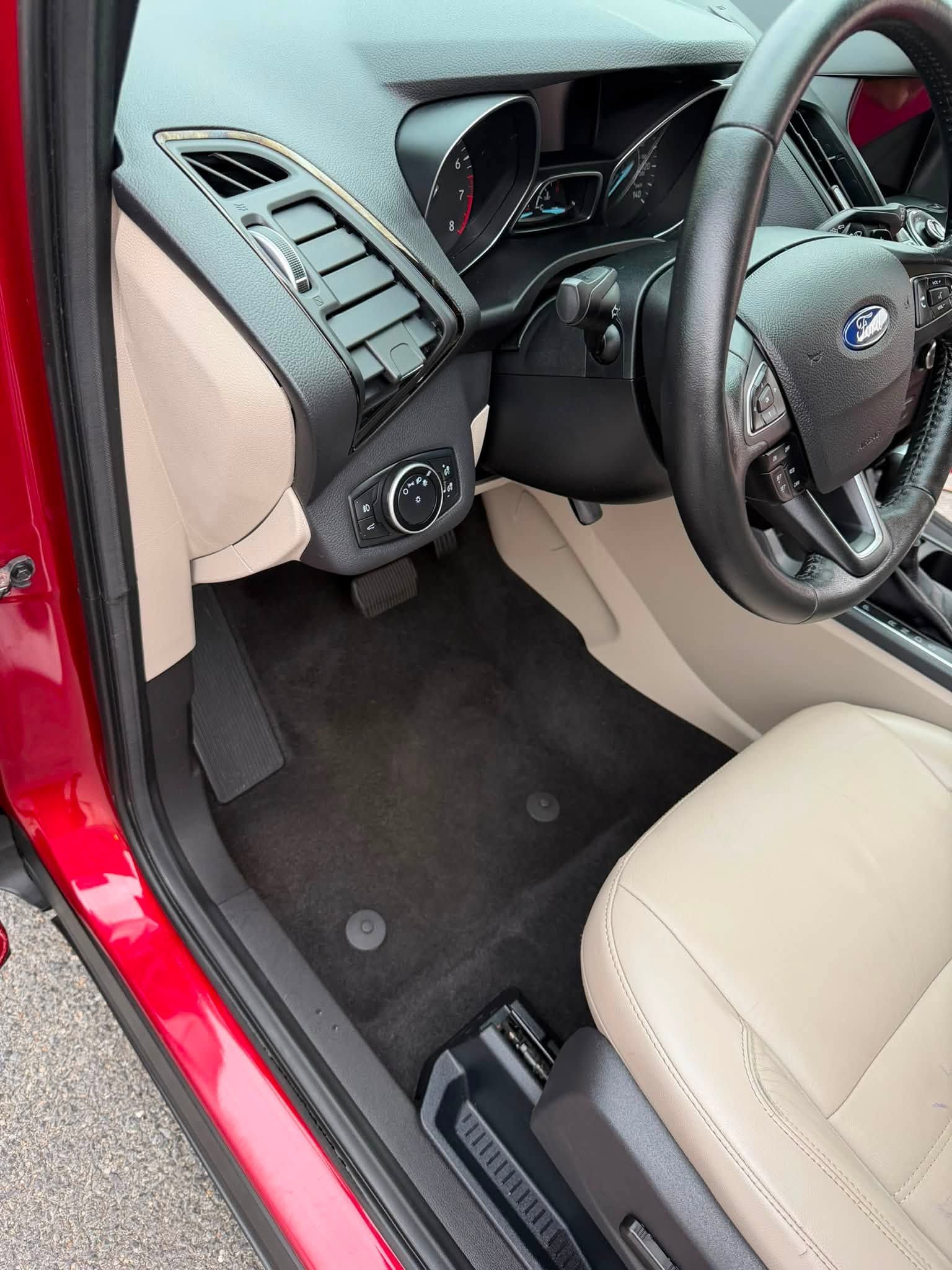 Driver-side view of a beige and black car interior with steering wheel and dashboard visible