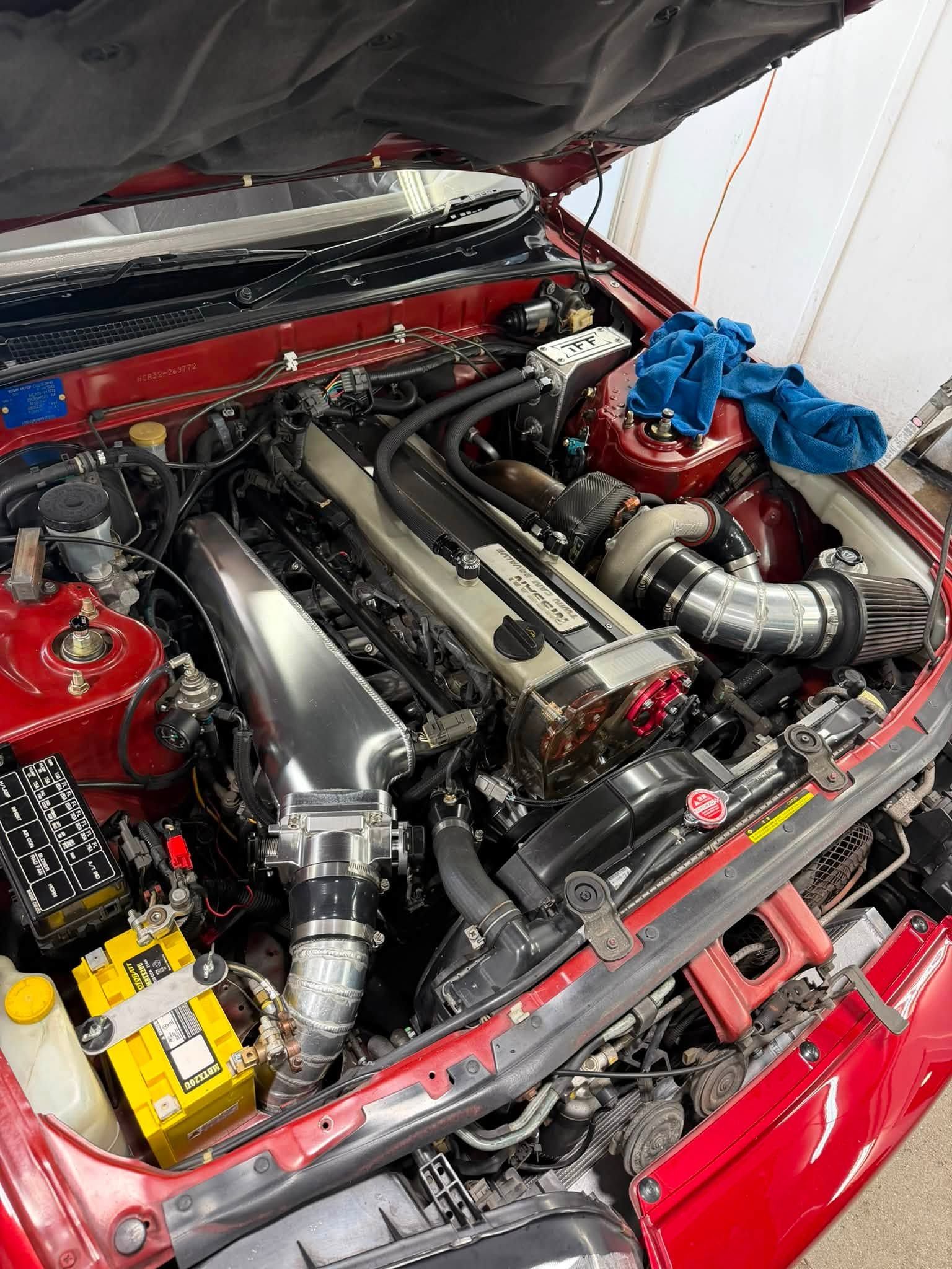 Car engine bay with polished intake piping, red body panels, and a blue engine cover open under the hood