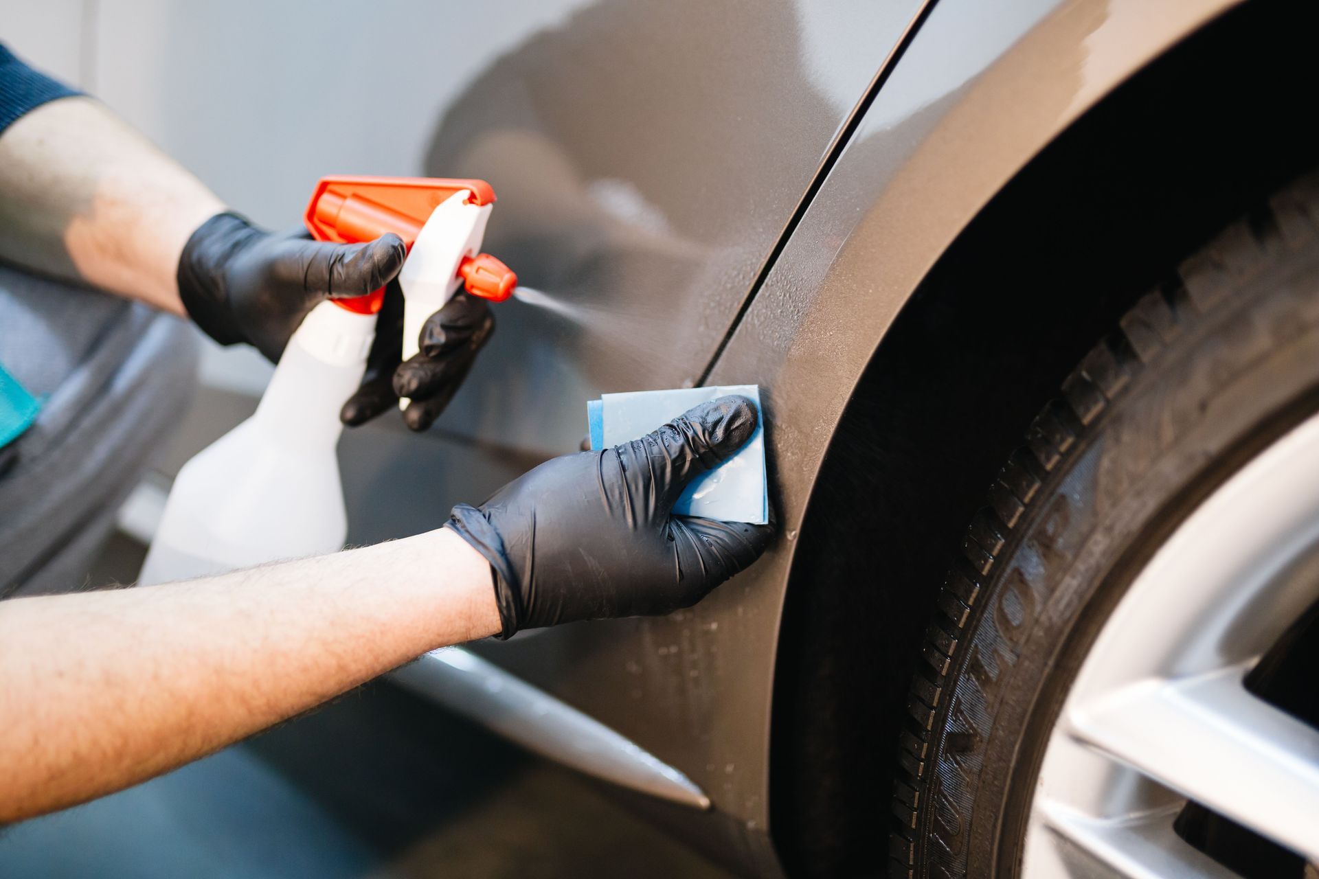 Gloved hands cleaning a car door with a spray bottle and cloth during detailing
