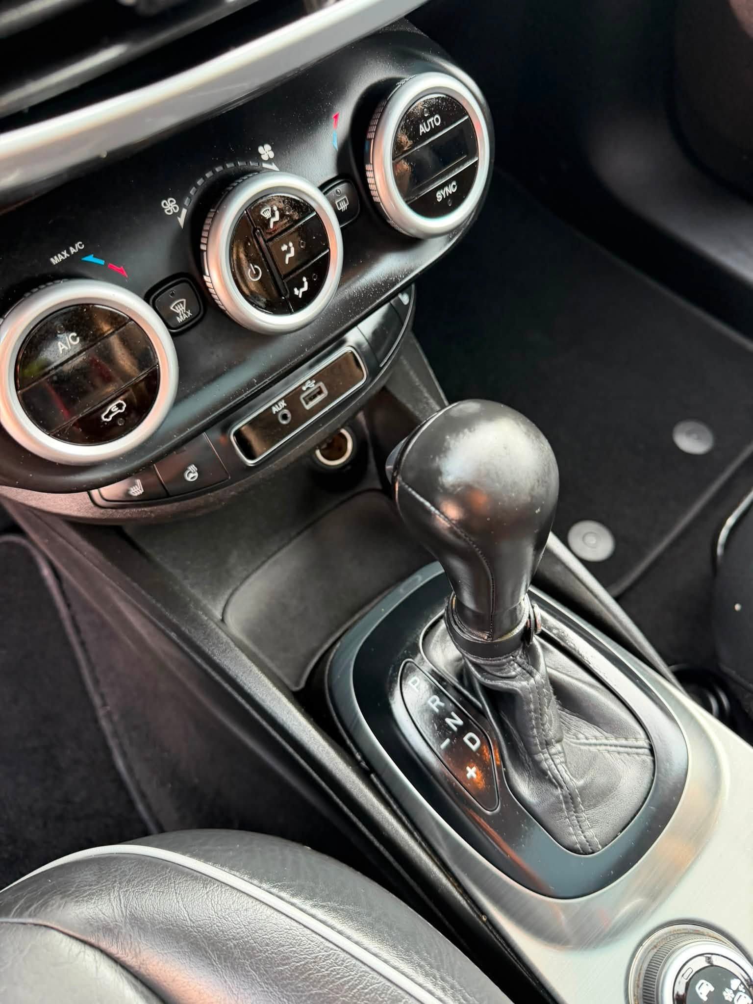 Car interior showing a black automatic gear shift and three circular climate control dials.