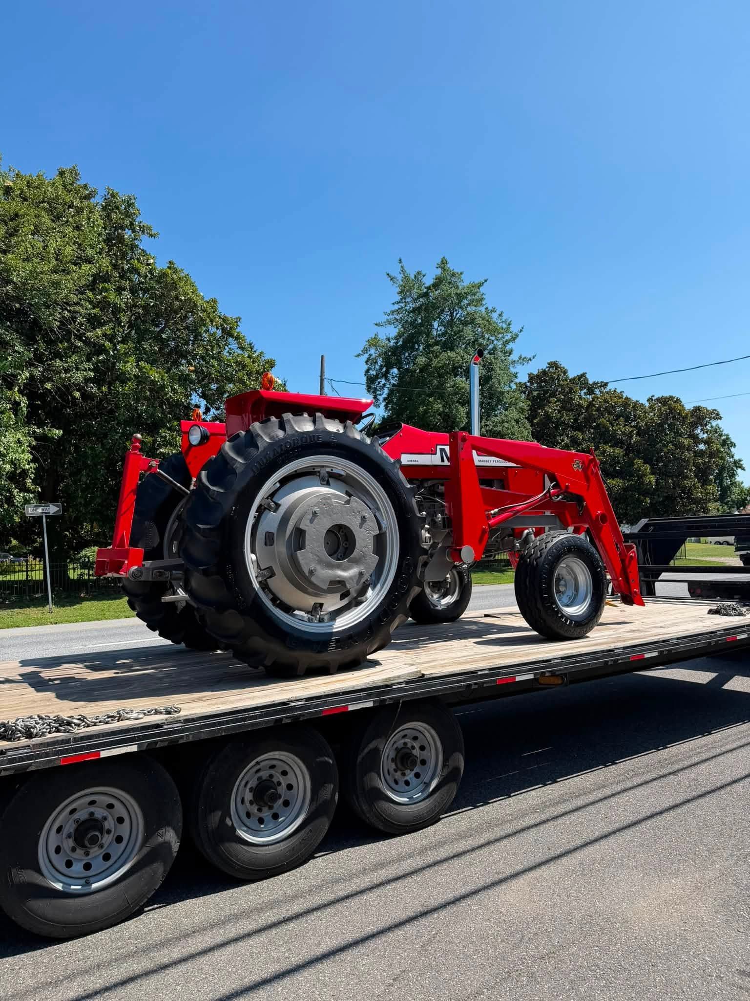Red tractor on a flatbed trailer on a road under a clear blue sky, with trees in the background